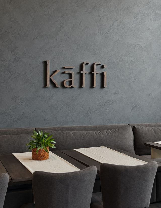 The Kāffi wordmark in wood on a plaster wall above banquette seating, Colombo 03